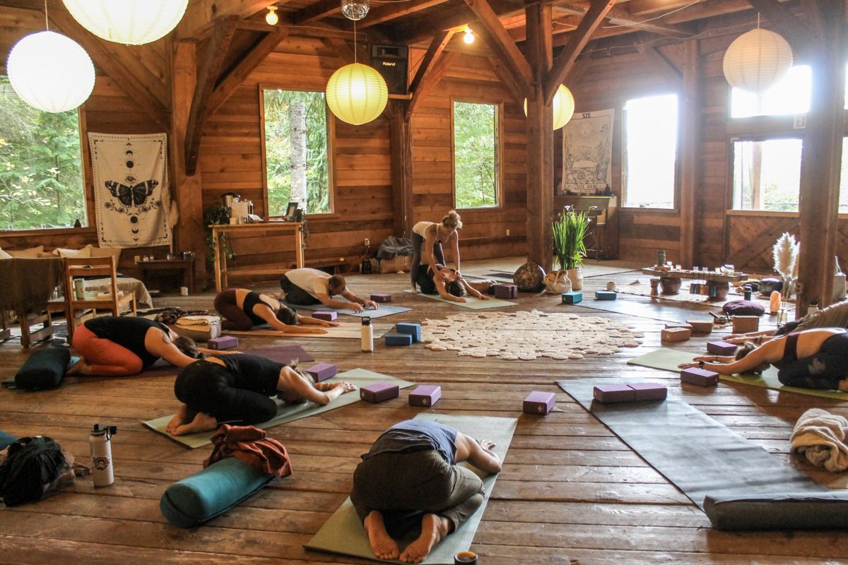 A yoga class resting in child's pose in a sunlit wooden hall